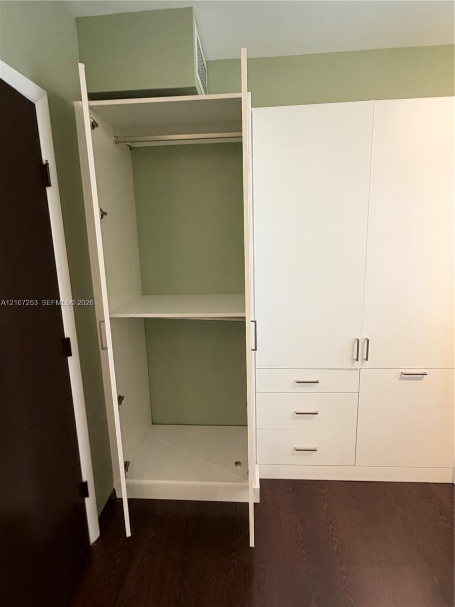 Built-in white cabinetry featuring adjustable shelving, a hanging rod, and three lower drawers with metal hardware