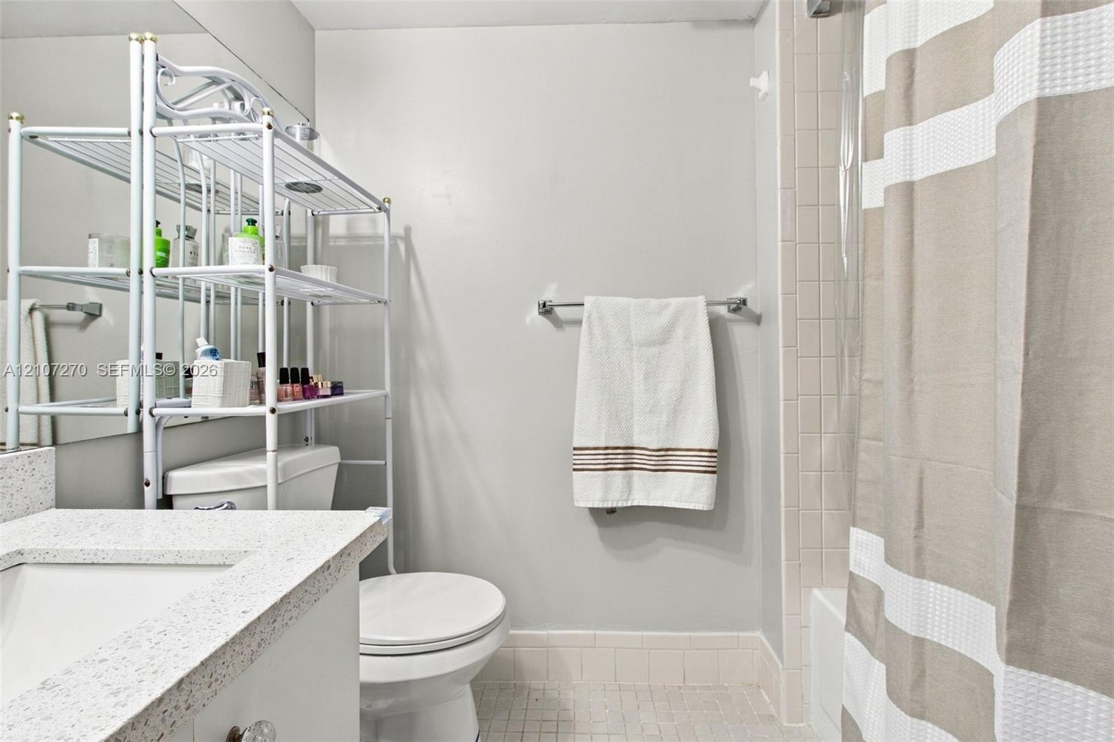 Bathroom featuring a vanity with a speckled countertop and integrated rectangular sink, wall-spanning mirror, ceramic tile shower surround, and tile flooring