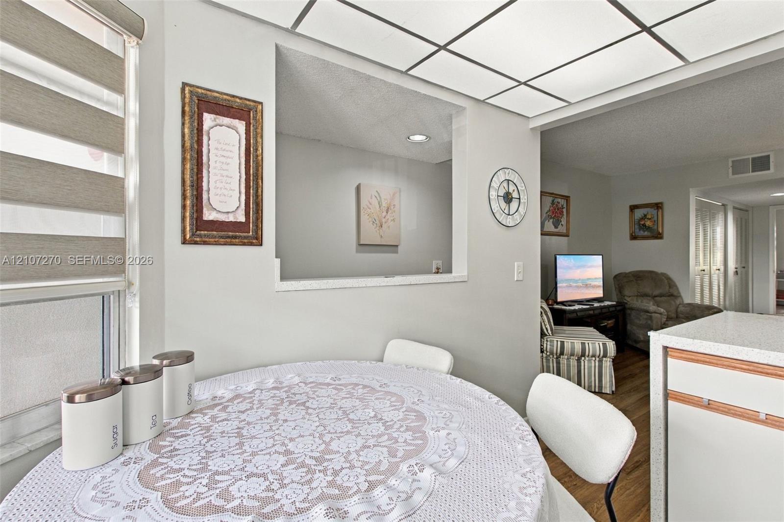 Pass-through window between rooms featuring a recessed opening, tray ceiling with inset panel lighting, tiered window shades, and solid surface countertop
