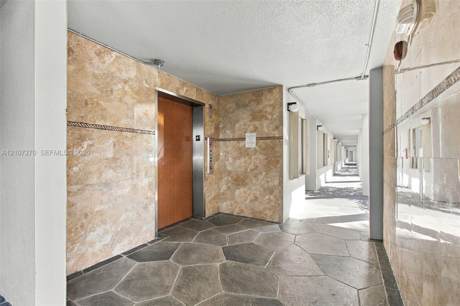Elevator lobby featuring polished stone wall cladding, decorative tile border accents, and flagstone-style flooring