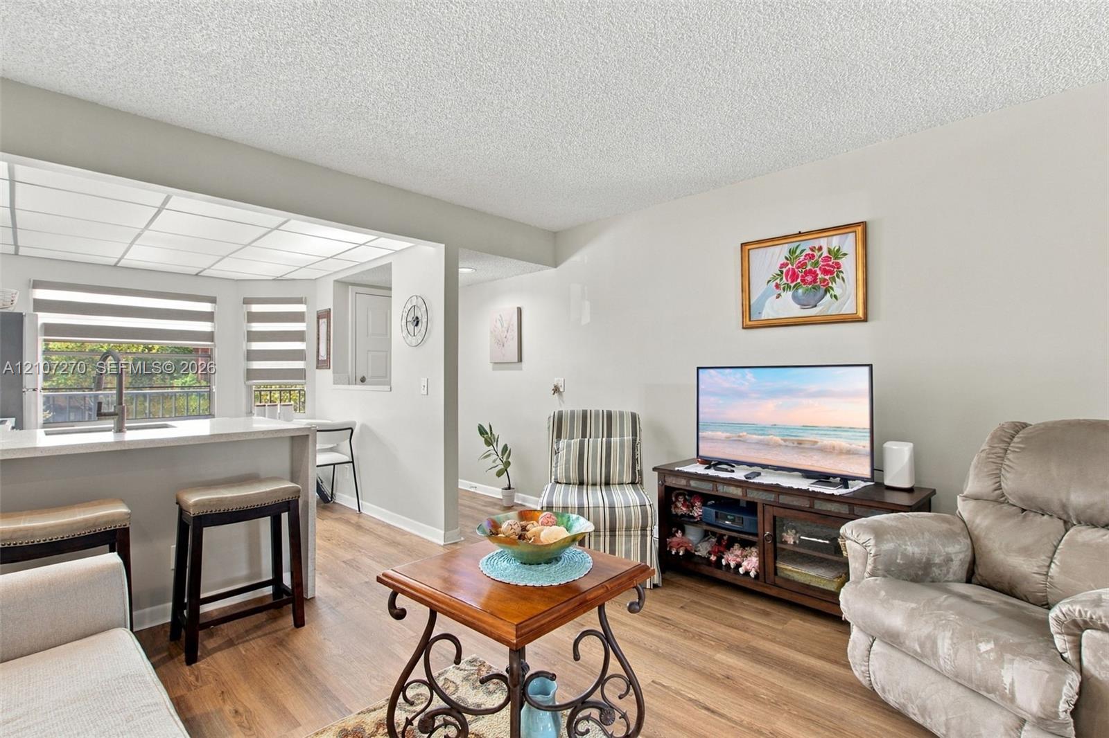 Open-concept interior featuring wood-finish flooring, a kitchen peninsula with a quartz countertop, and recessed ceiling panels with integrated lighting