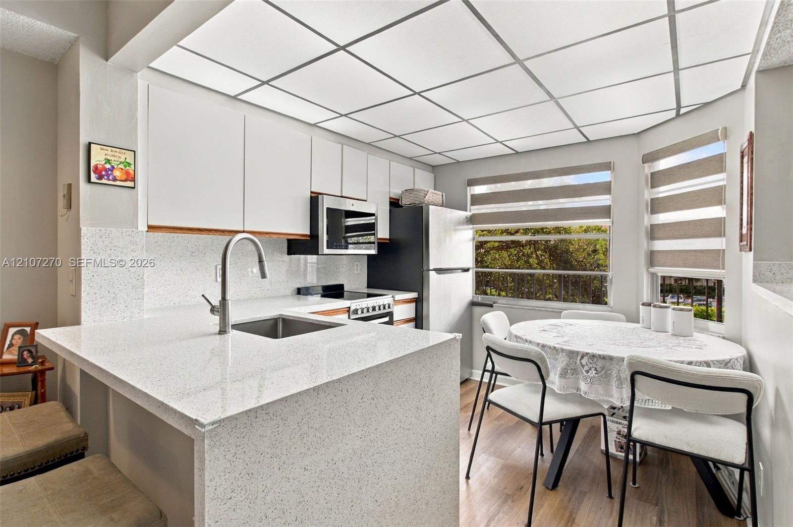 Kitchen featuring white flat-panel cabinetry, light-toned speckled countertops, a stainless steel undermount sink with a gooseneck faucet, wood-finish flooring, and a drop ceiling grid