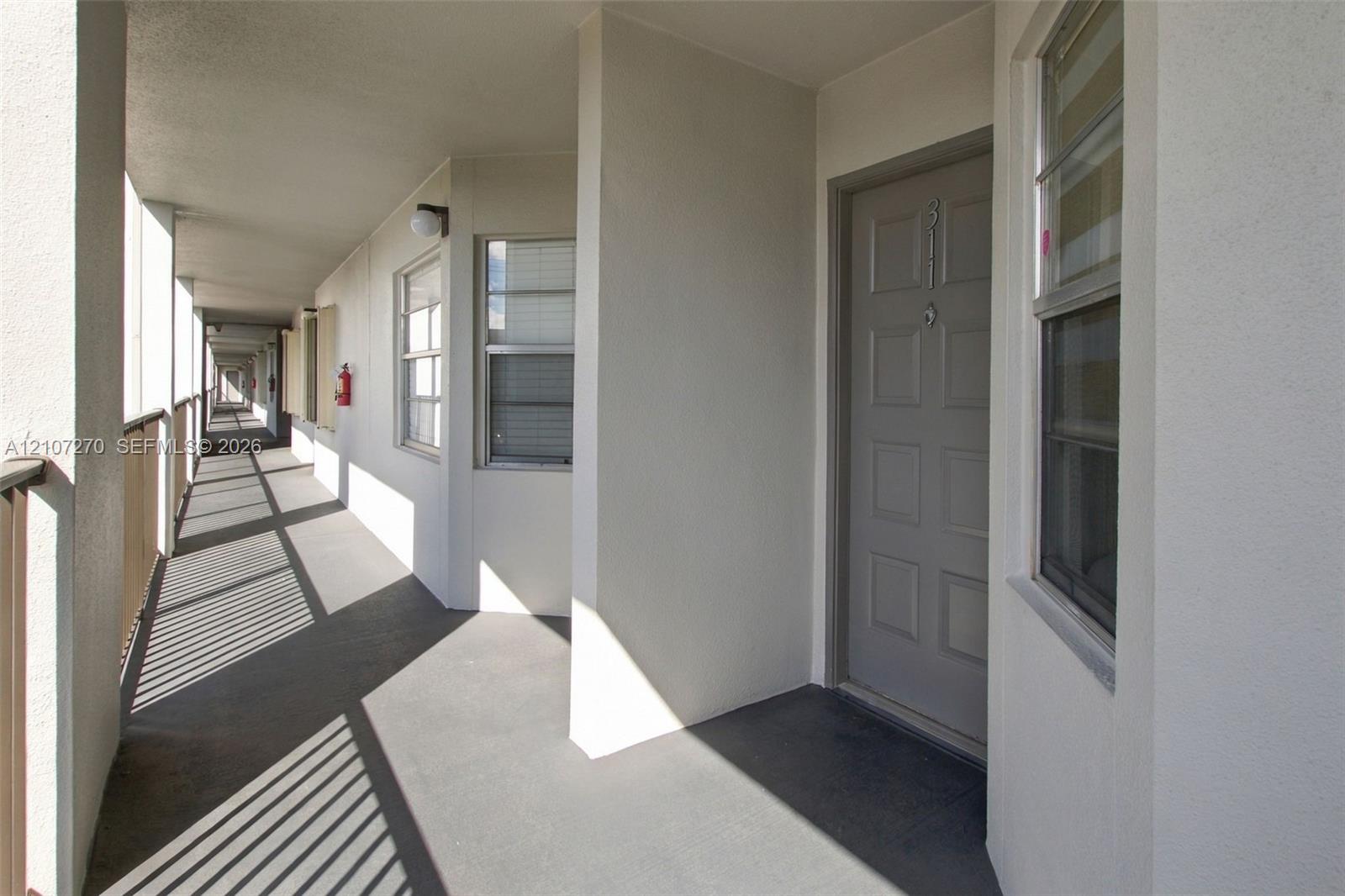 Exterior walkway featuring a six-panel door, neutral stucco walls, metal railings, and dual-pane windows