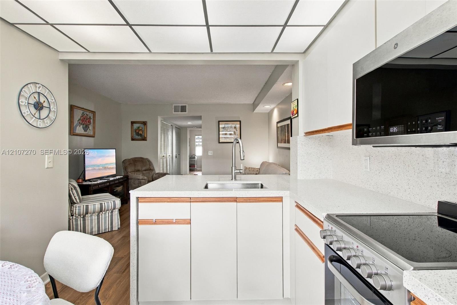 Kitchen featuring white cabinetry with wood-tone accents, solid surface countertops, stainless steel appliances, and a grid-style drop ceiling