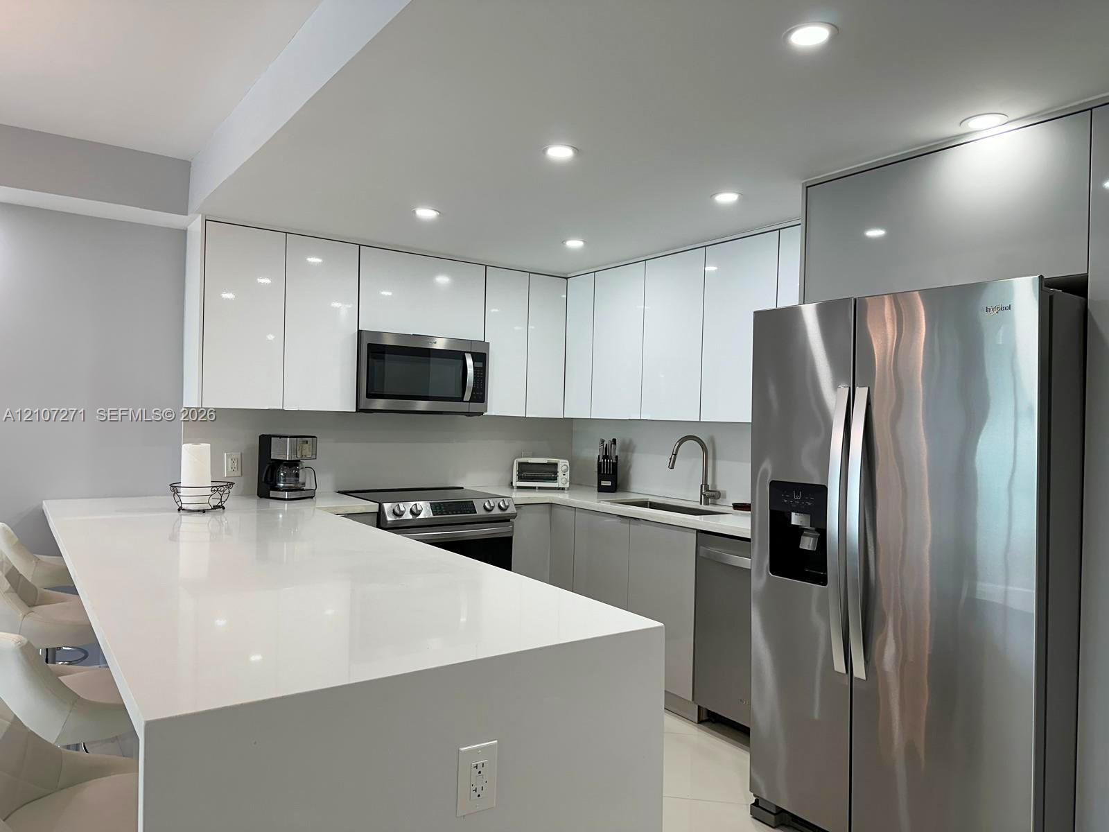 Kitchen featuring high-gloss cabinetry, a waterfall-edge countertop, stainless steel appliances, and recessed ceiling lighting