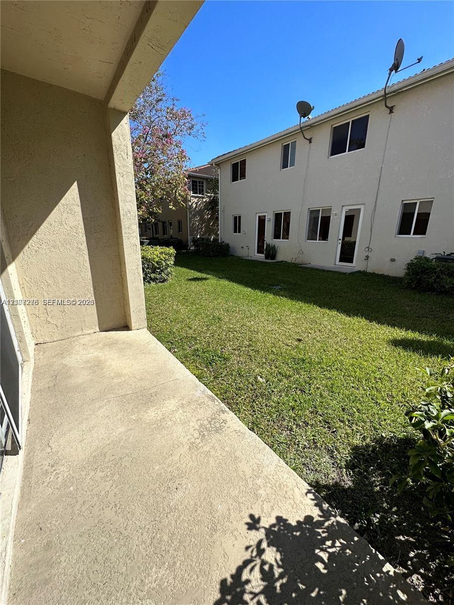Concrete patio slab extending toward a lawn area with perimeter shrubbery and stucco exterior finish