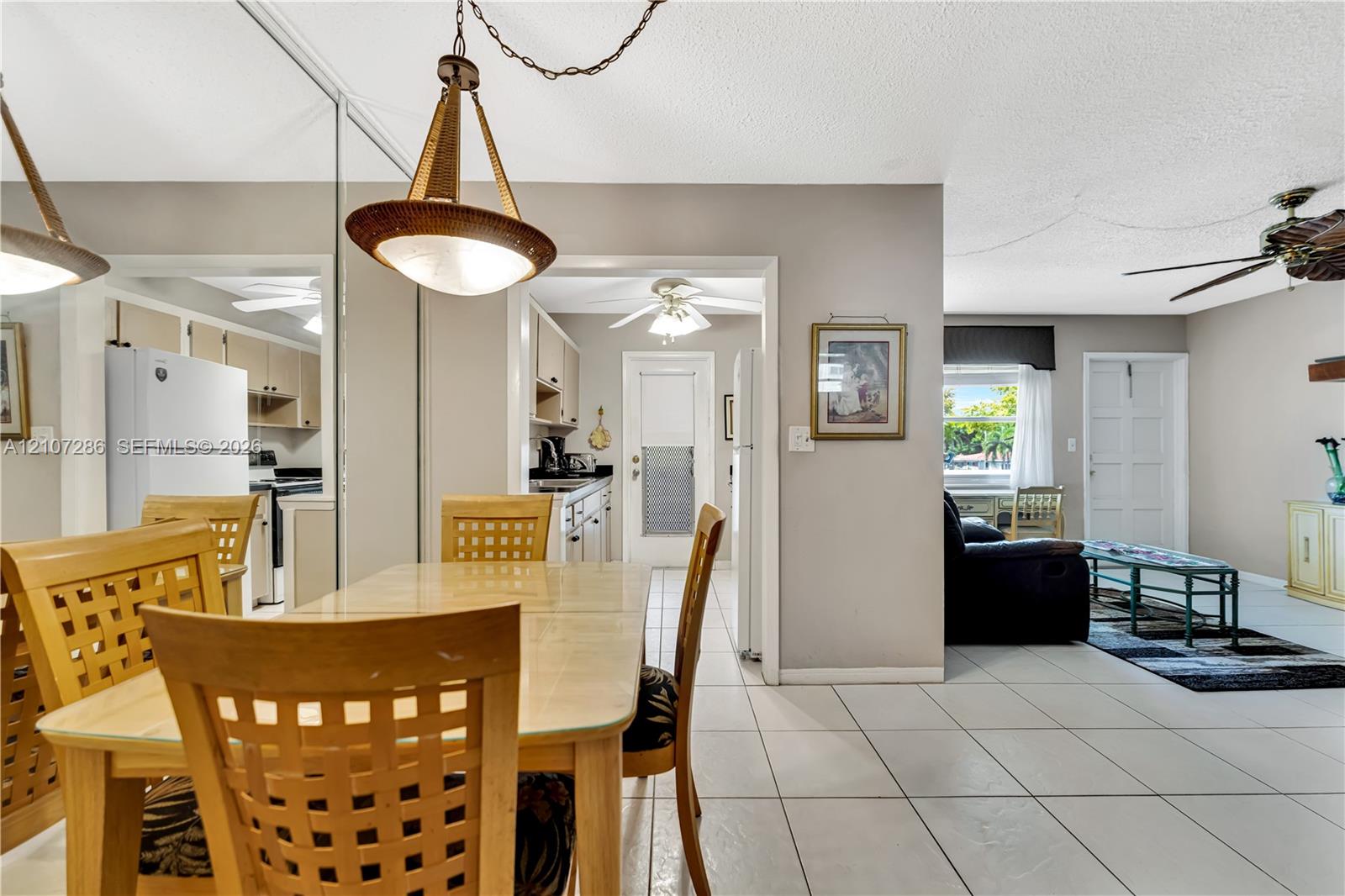 Open-concept interior featuring oversized wall mirrors, neutral tile flooring, a multi-light pendant fixture, ceiling fans, and a classic paneled exterior door