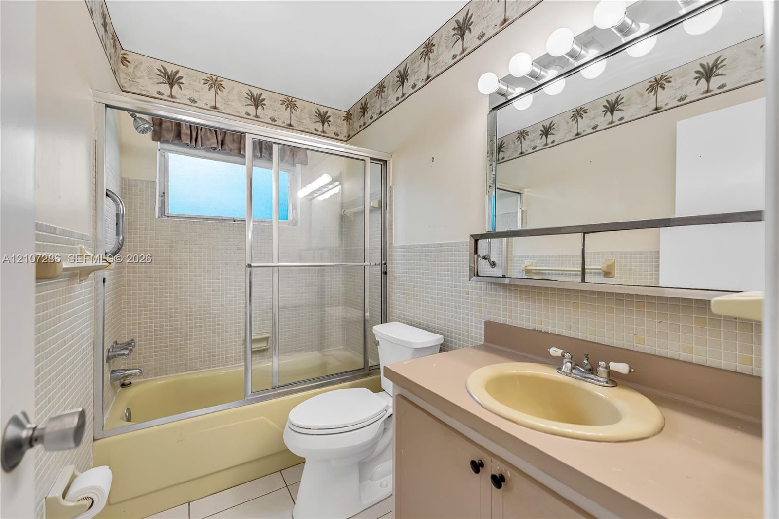 Bathroom featuring a shower and tub combination with sliding glass doors, vanity with an integrated basin, wall-mounted mirror, and tile wall surfacing