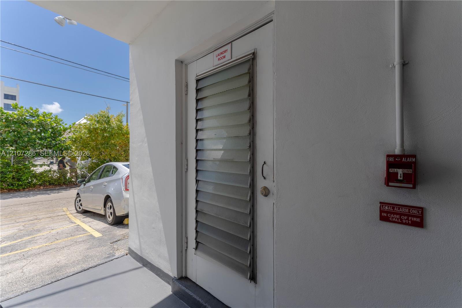 Exterior door featuring integrated jalousie window panels, smooth stucco wall finish, and a mounted fire alarm system