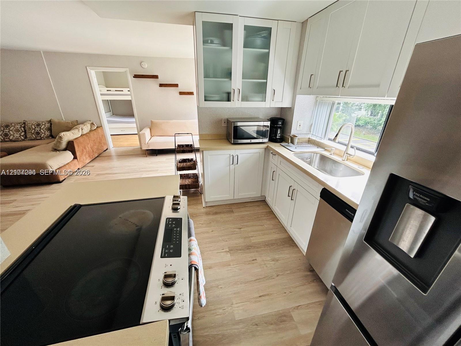 Kitchen featuring white cabinetry, glass-front upper cabinets, stainless steel appliances, and wood-finish flooring