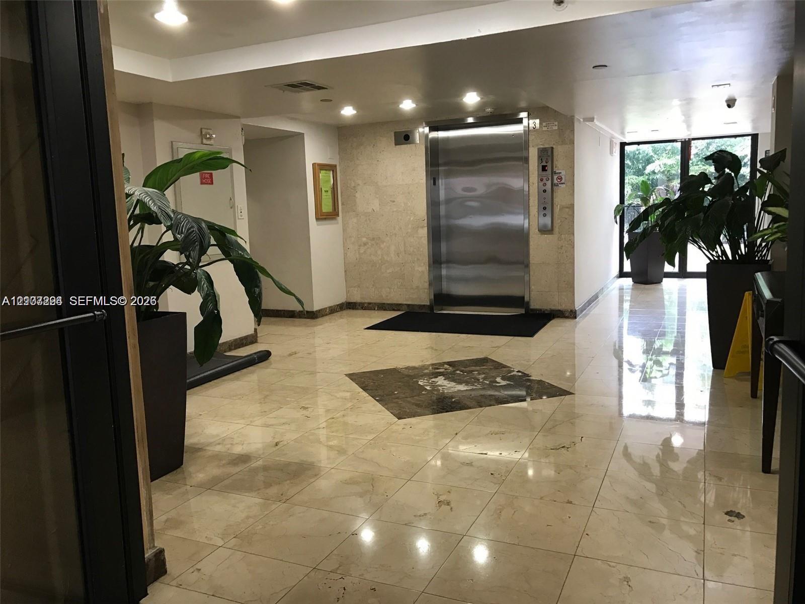 Elevator lobby featuring polished stone flooring with an inlaid stone medallion, recessed lighting, and a stainless steel elevator door