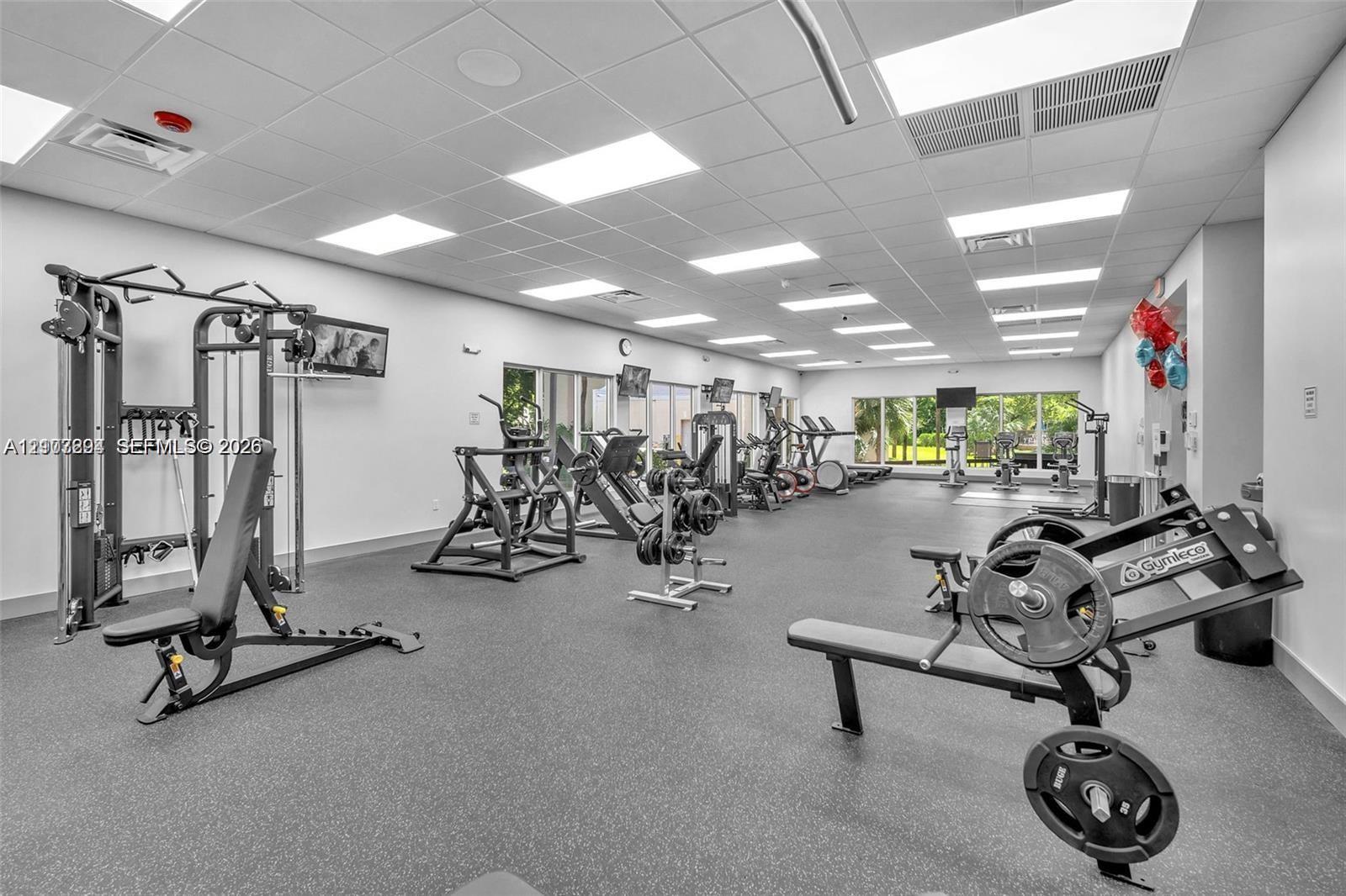Fitness center featuring recessed drop-ceiling lighting, resilient rubberized flooring, and expansive windows