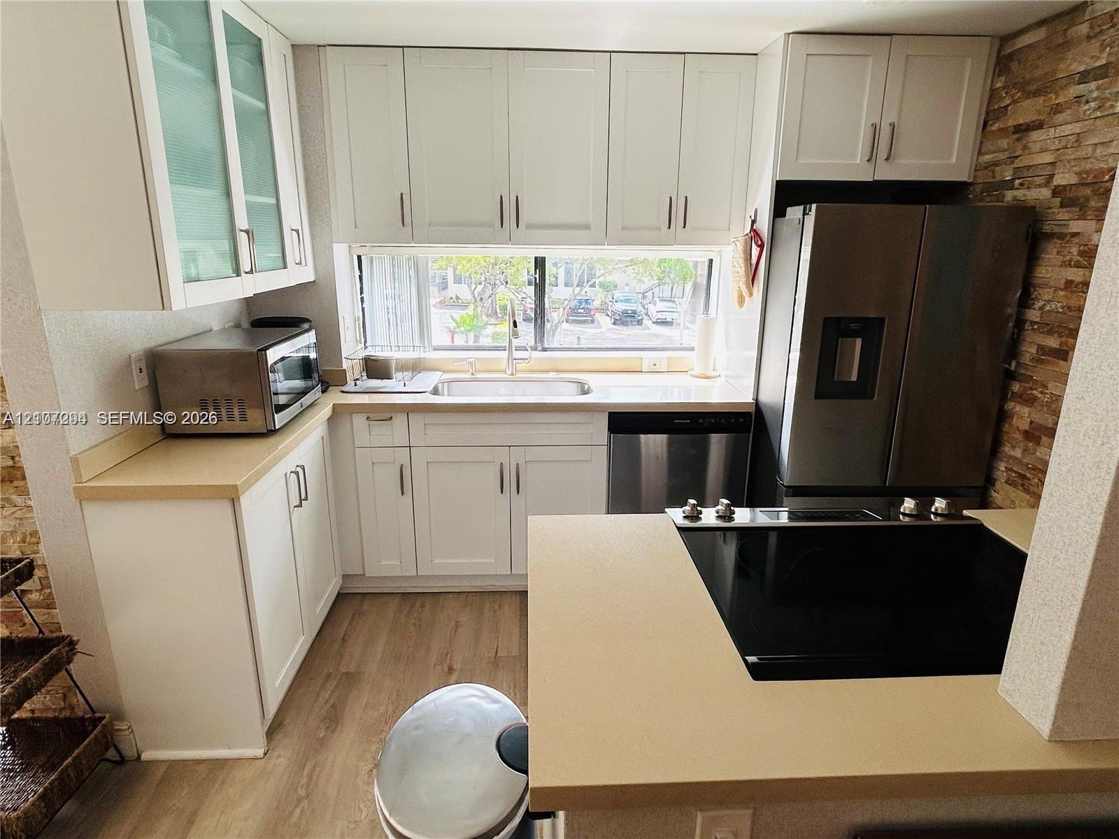 Kitchen featuring white shaker-style cabinetry, solid-surface countertops, wood-finish flooring, a stainless steel refrigerator, and a stacked stone accent wall