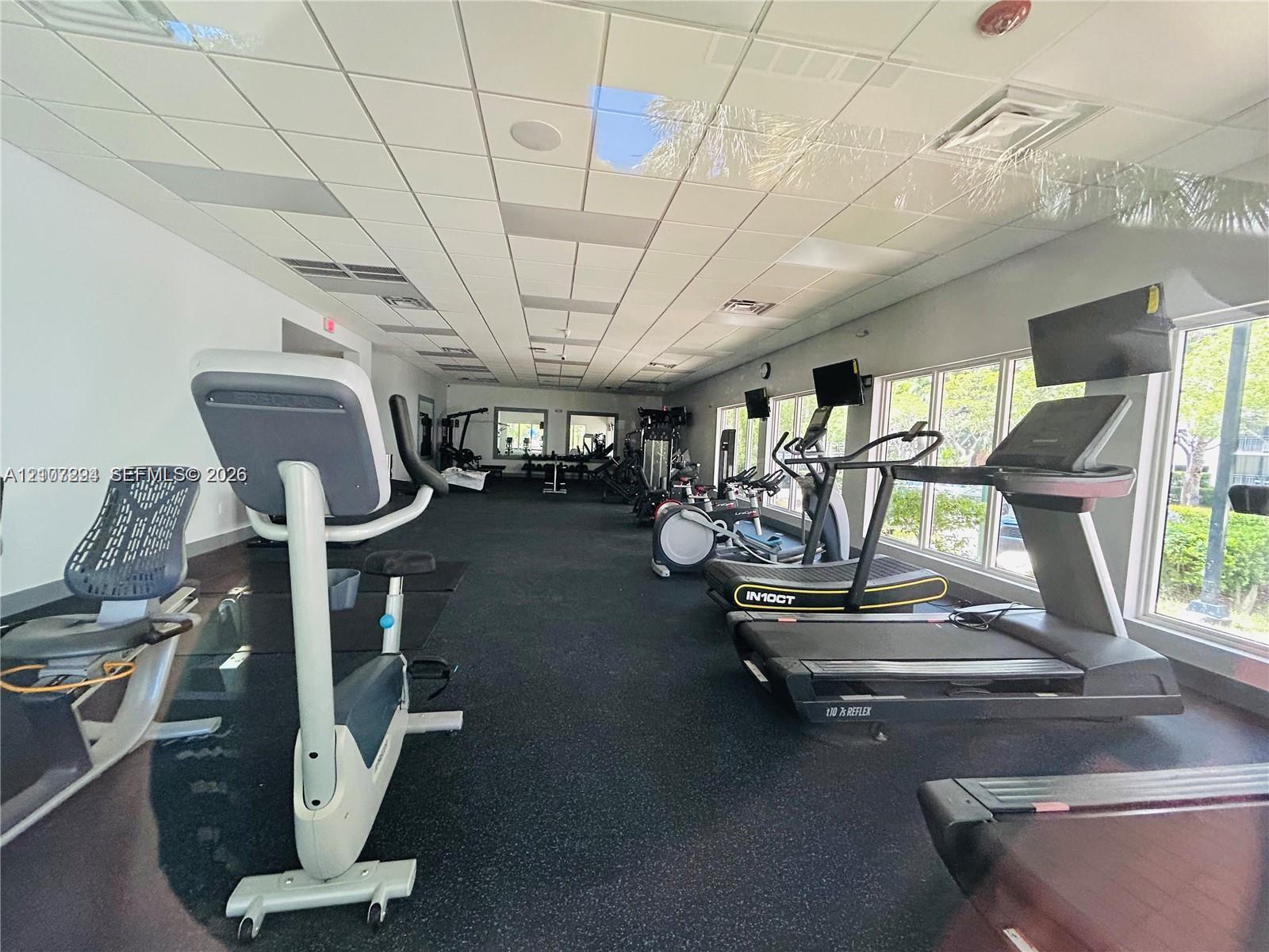 Fitness room featuring high-impact rubber flooring, drop ceiling with recessed lighting, and large windows