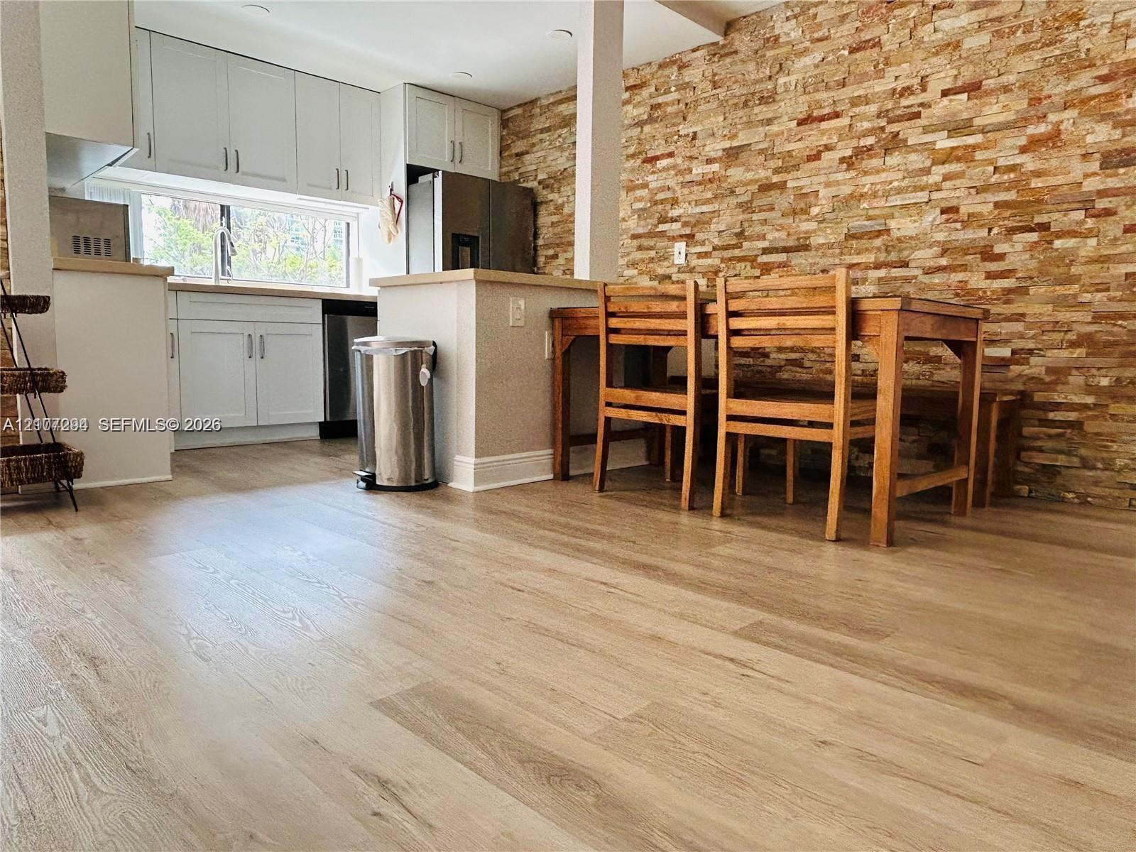 Kitchen featuring white shaker-style cabinetry, a stacked stone accent wall, and light wood-finish flooring
