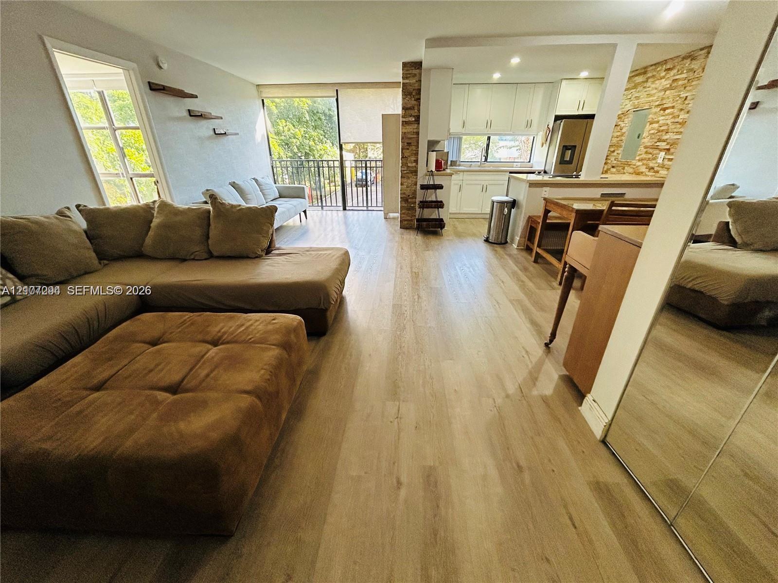 Open-concept interior featuring wood-finish flooring, textured stone accent wall, recessed lighting, white cabinetry, and balcony access