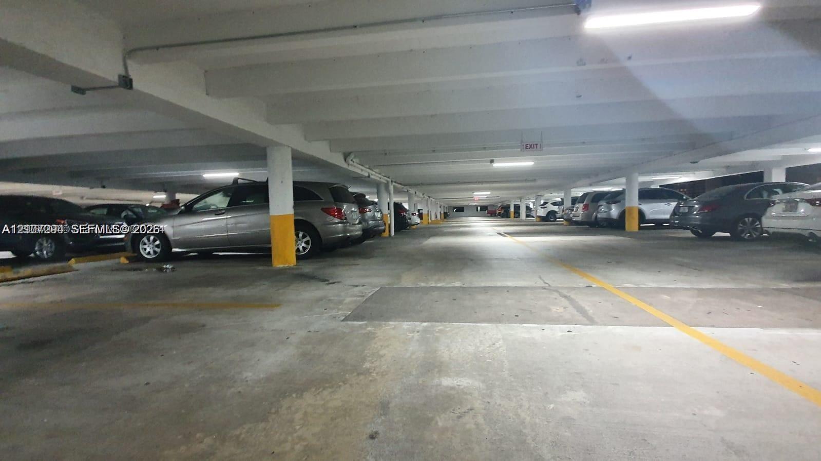 Covered parking garage featuring concrete flooring, structural support columns, and overhead lighting