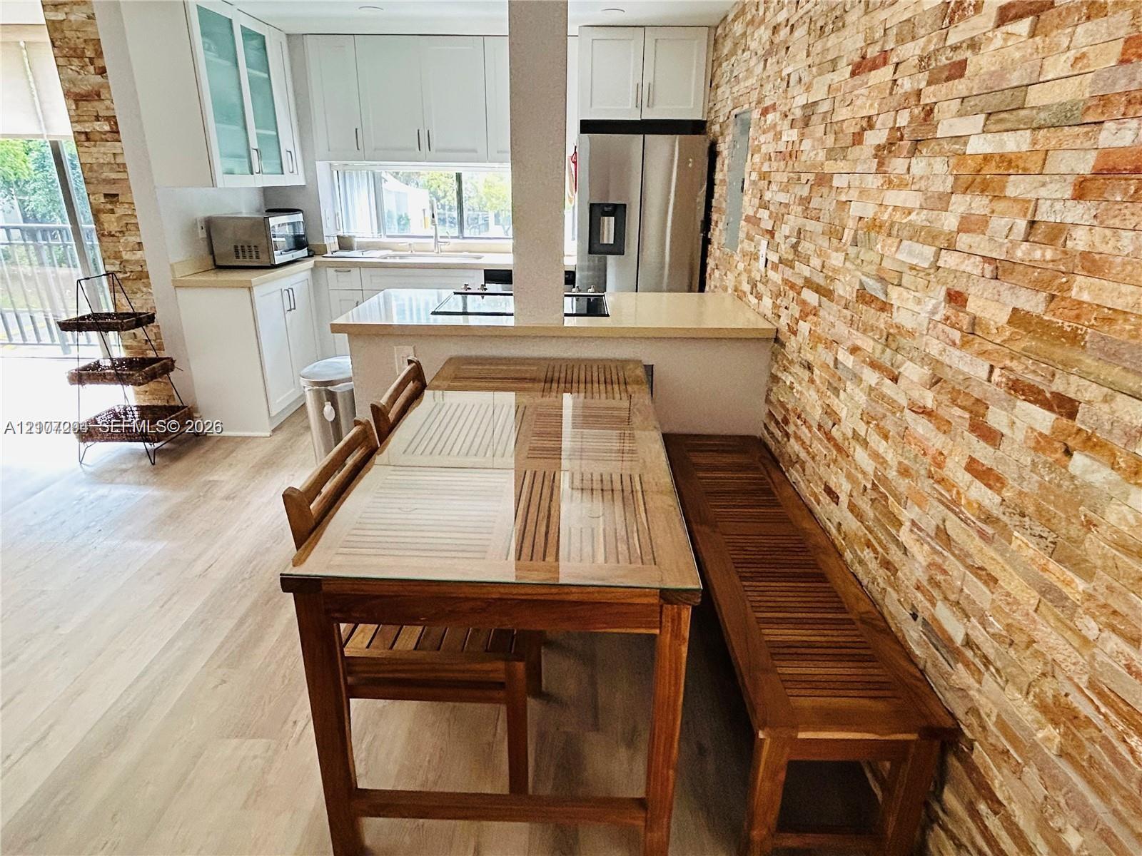 Kitchen featuring white cabinetry, solid-surface countertops, stone-veneer accent wall, and wood-finish flooring