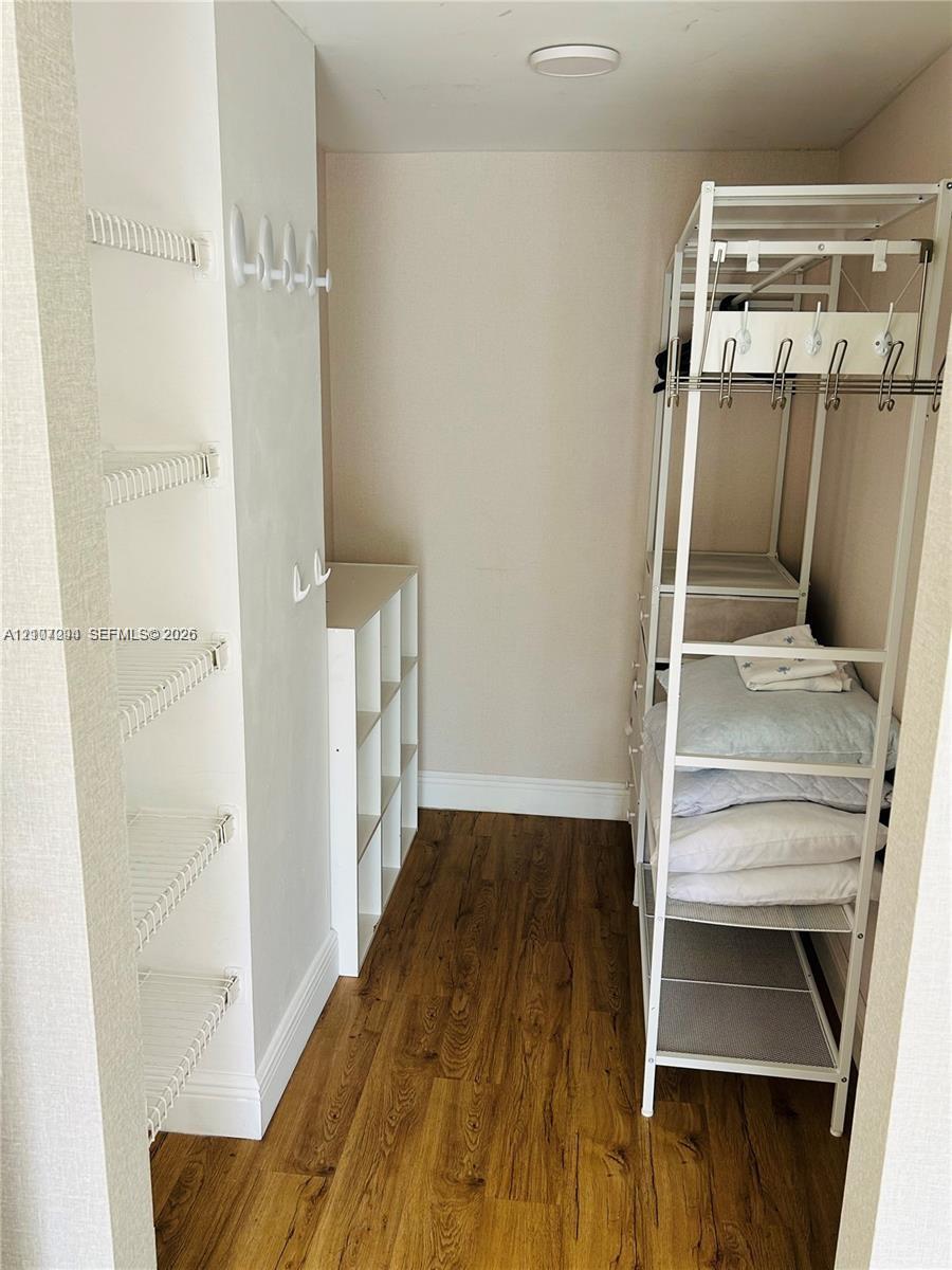 Storage space featuring wood-finish flooring, white wire wall shelving, integrated wall-mounted hooks, and a white laminate cubby unit