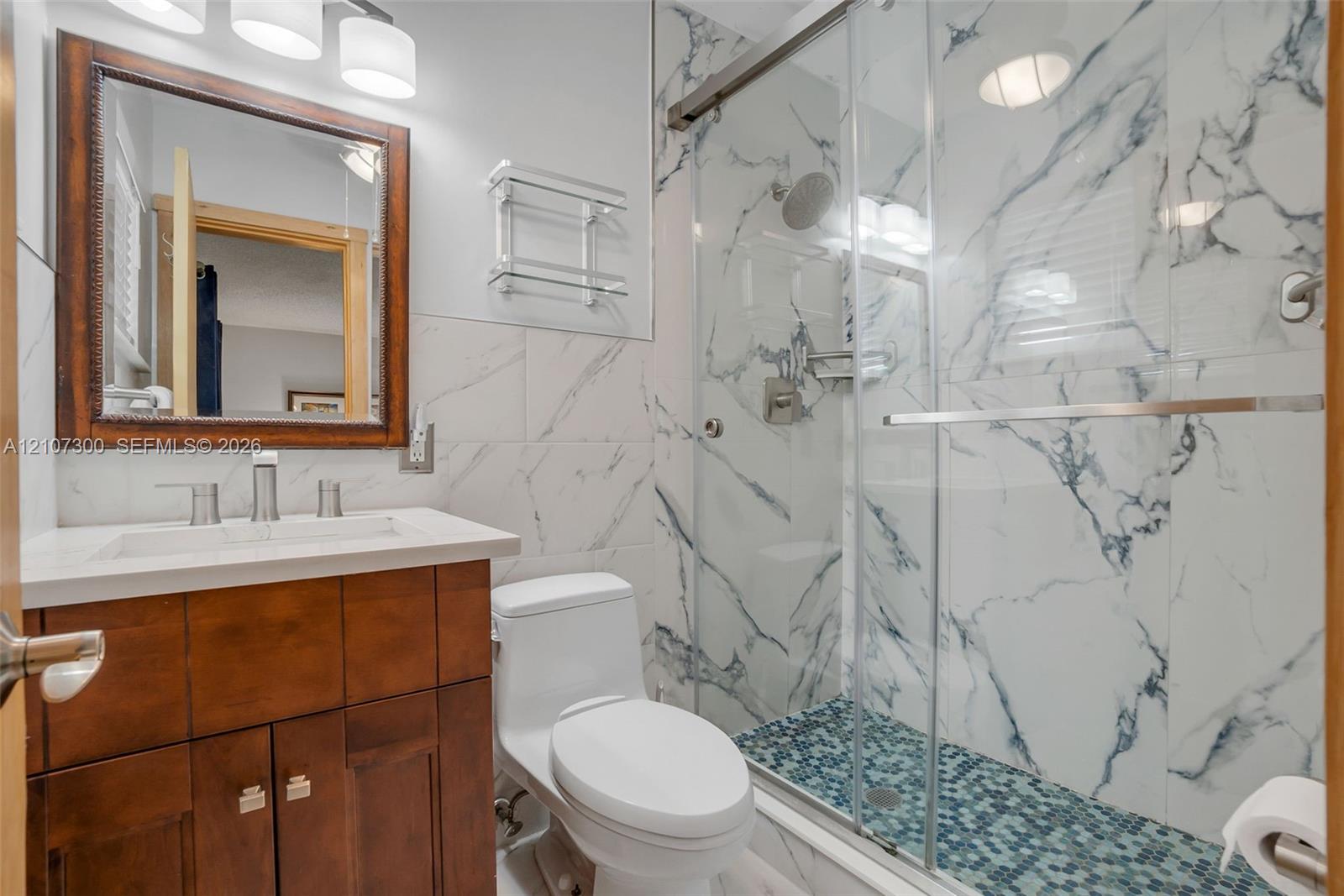 Bathroom featuring a dark wood vanity with white countertop, rectangular undermount sink, shower with glass sliding door and large-format tile surround, and mosaic tile shower floor
