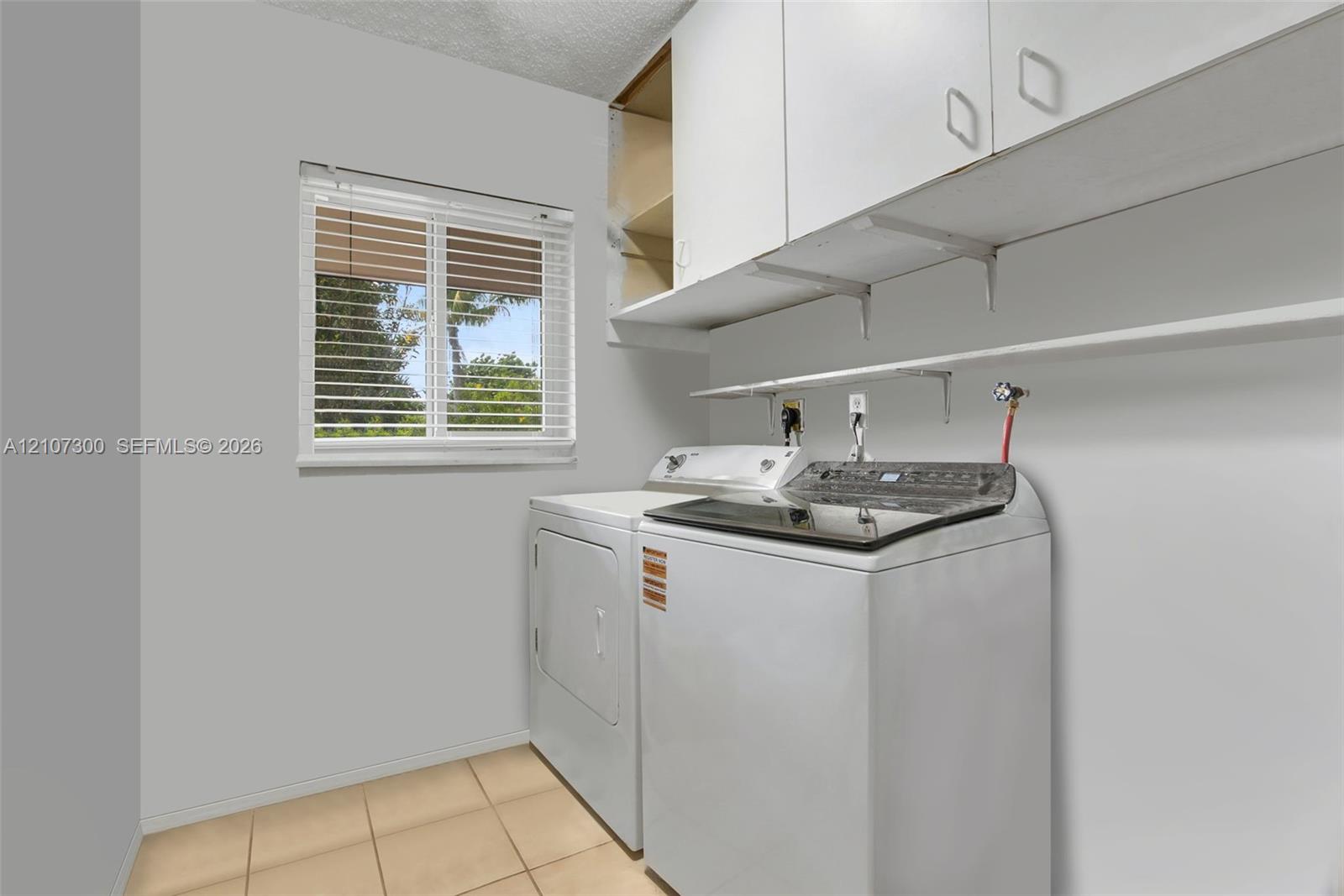 Utility area featuring overhead cabinetry, open shelving, tile flooring, and a single-pane window with horizontal blinds