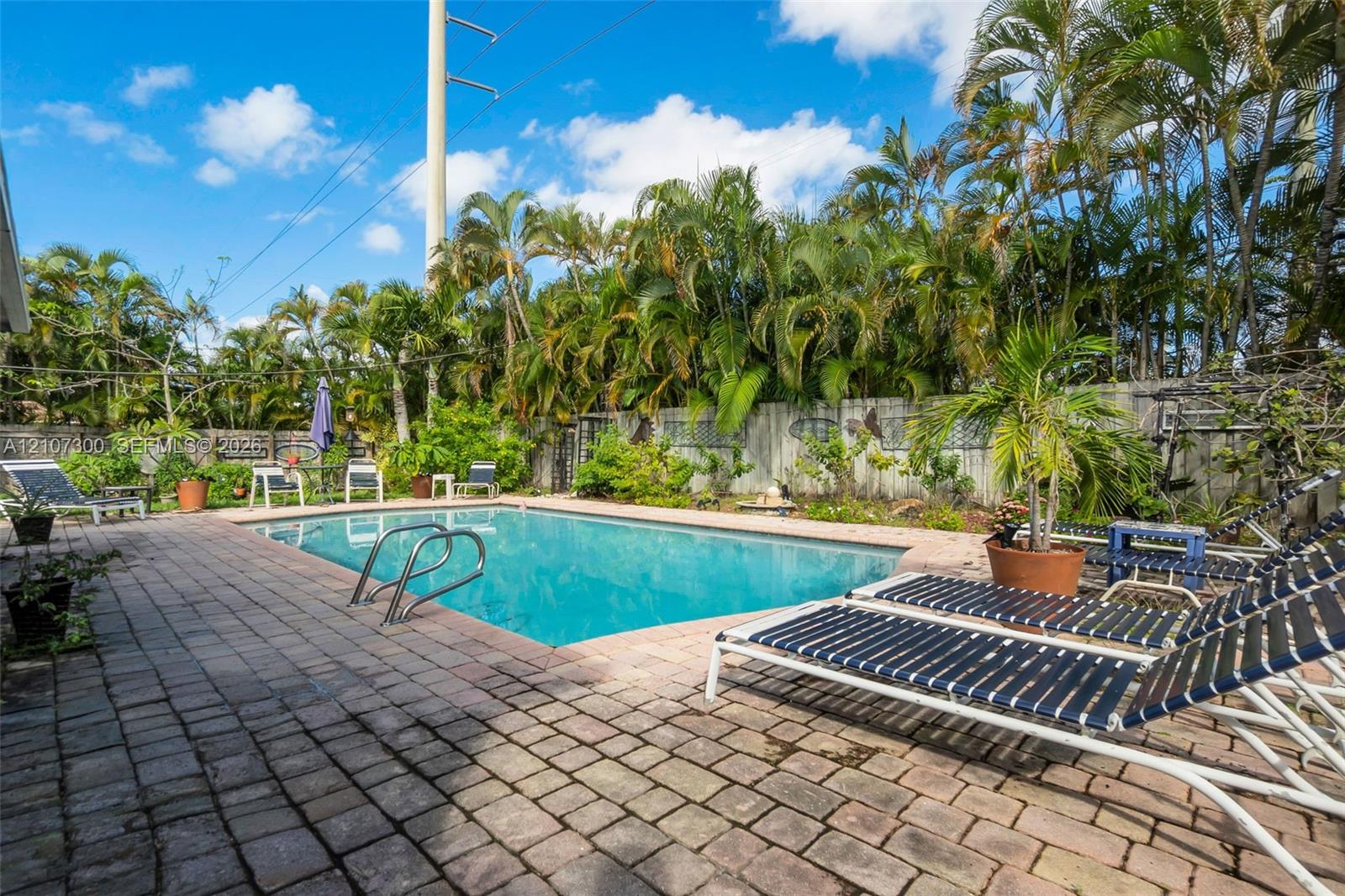 In-ground swimming pool with metal ladder entry, surrounded by a brick-paver patio and privacy fencing