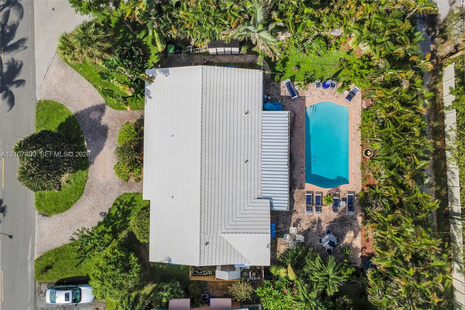 Aerial view featuring a metal roof, paver driveway, swimming pool, paver patio, and mature perimeter landscaping