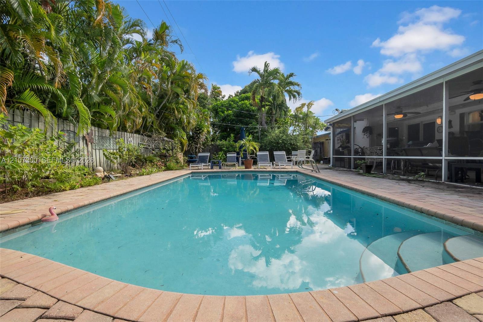 In-ground swimming pool with brick paver coping, screened-in lanai, and lush perimeter landscaping