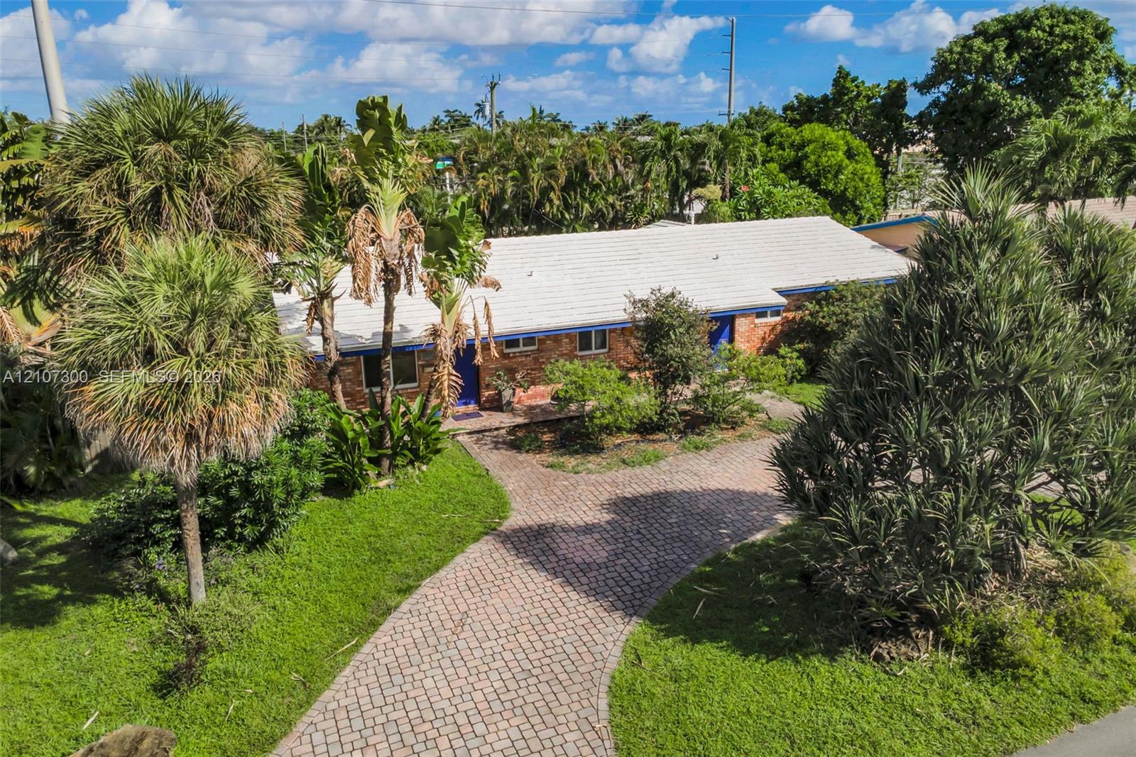 Single-story residence featuring a brick facade, light-toned shingle roof, and a paved stone driveway, surrounded by established landscaping