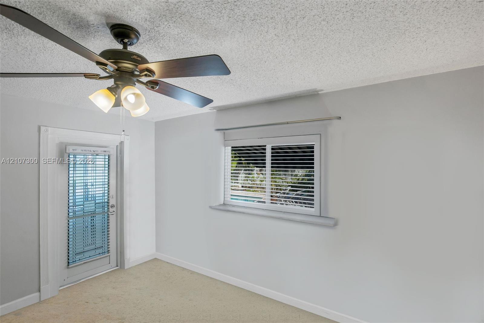 Neutral interior featuring a ceiling fan with integrated three-light fixture, single-panel exterior door with glass insert, horizontal window blinds, and carpeted flooring