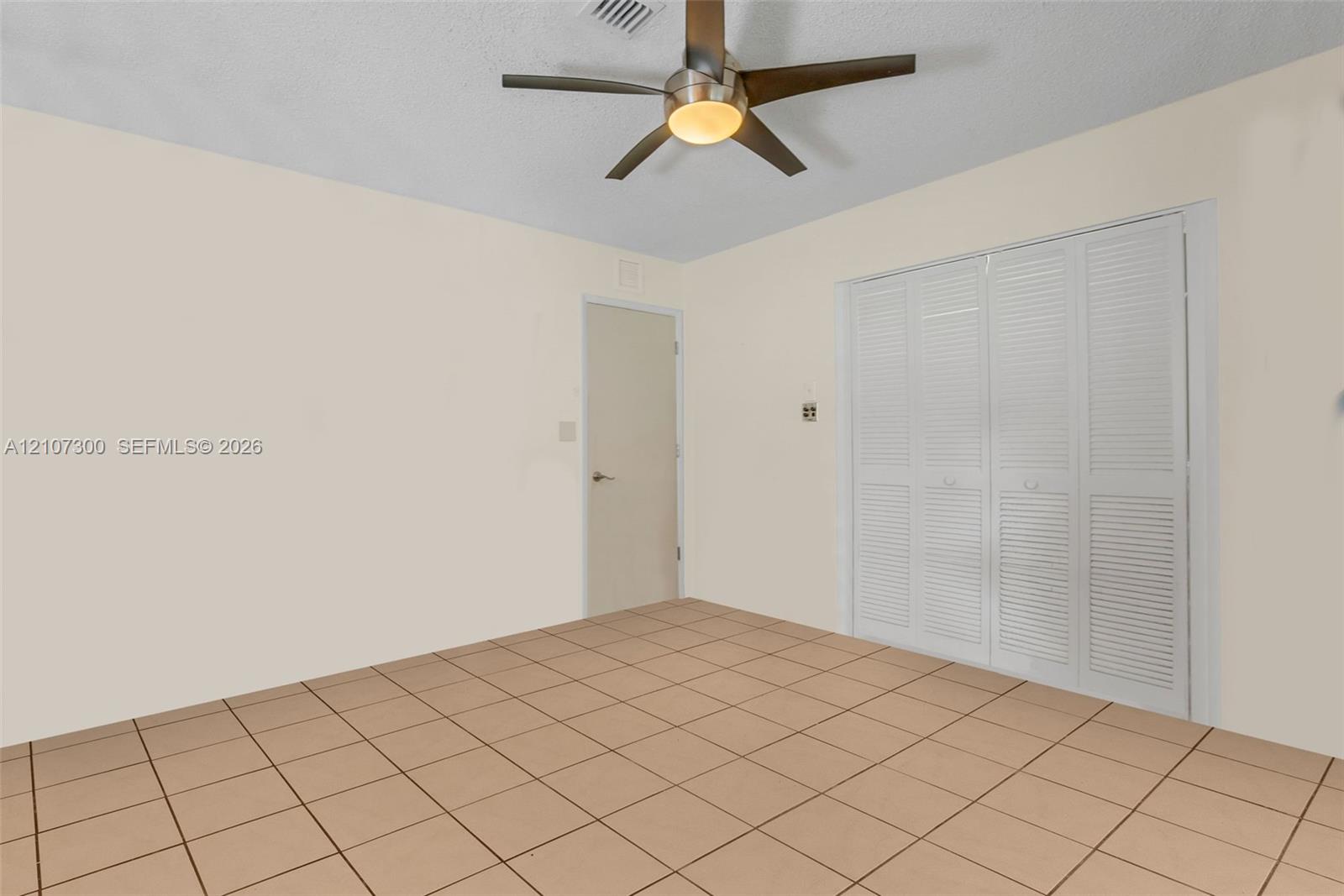 Room featuring ceramic tile flooring, a brushed-metal ceiling fan with integrated lighting, and white louvered-style closet doors