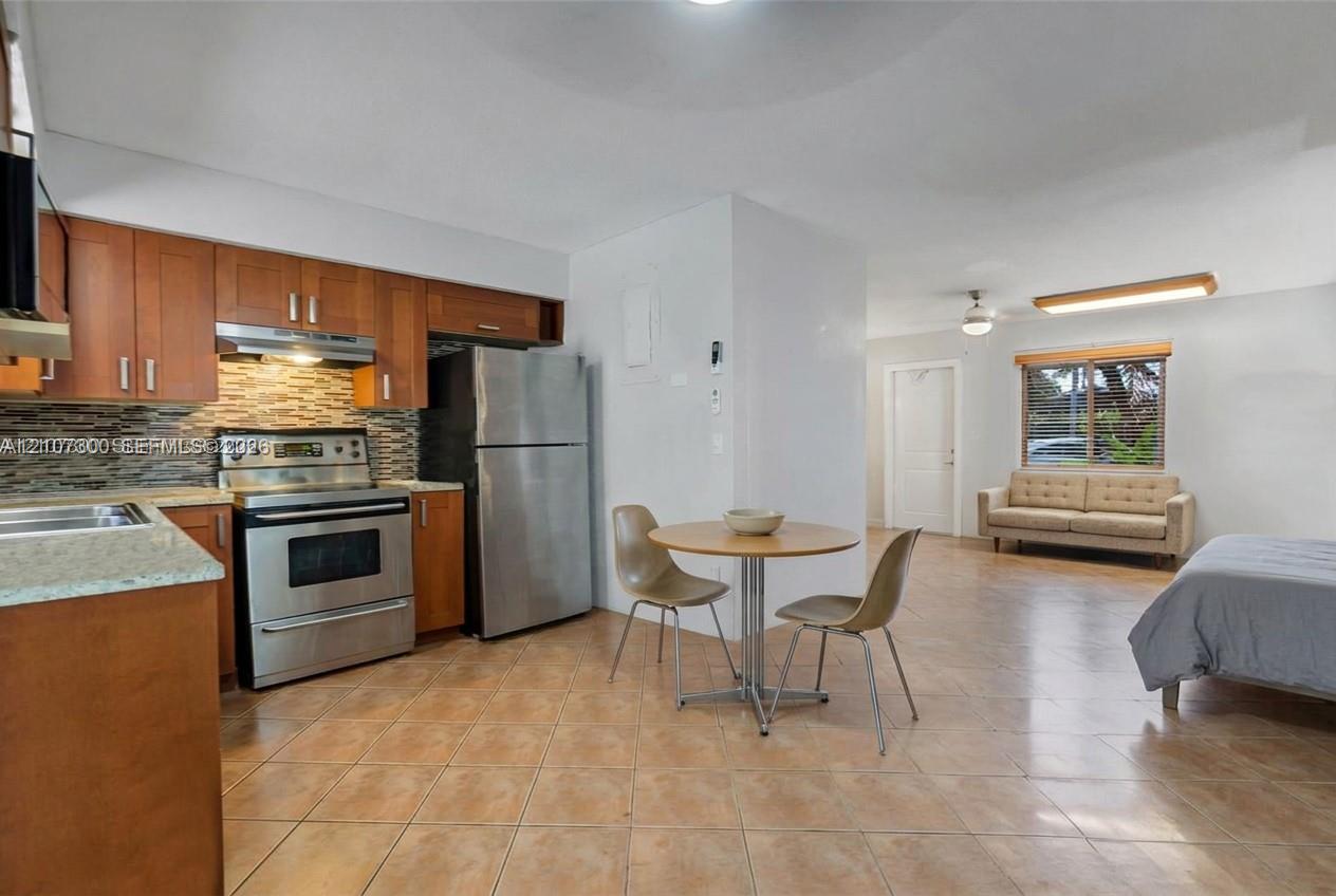 Kitchen featuring flat-panel wood cabinetry, stone countertops, a mosaic tile backsplash, and stainless steel appliances, set against tile flooring
