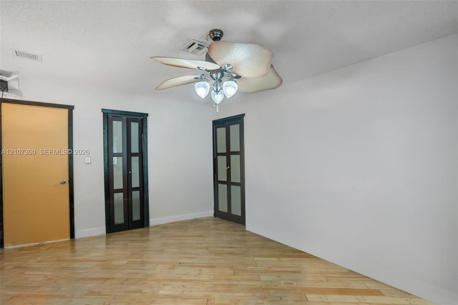 Interior space featuring wood-finish flooring, a multi-blade ceiling fan with integrated lighting, and dual four-panel glass-inset doors with dark frames