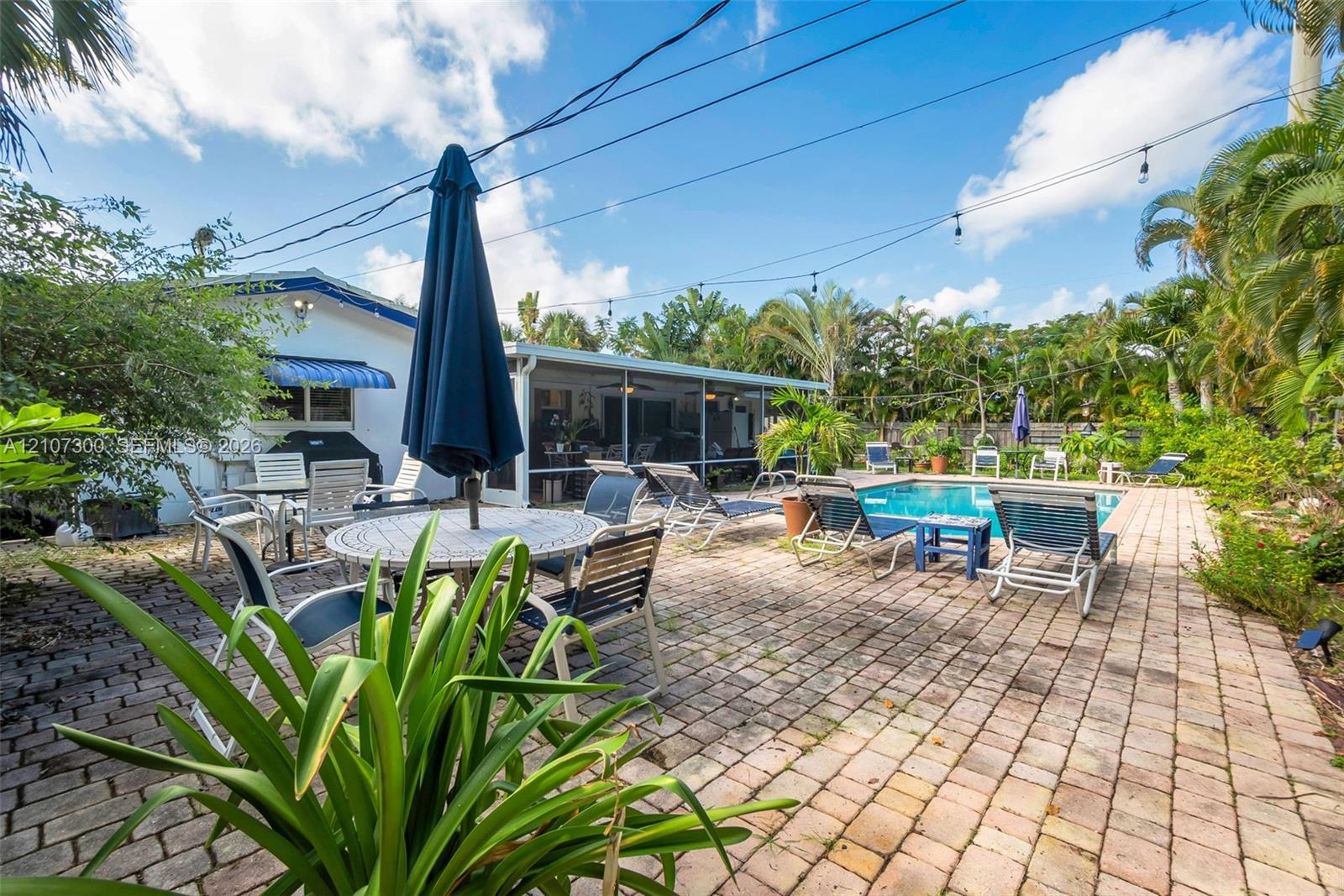 Outdoor living space featuring a paver patio, screened-in lanai, and an in-ground swimming pool surrounded by mature palms