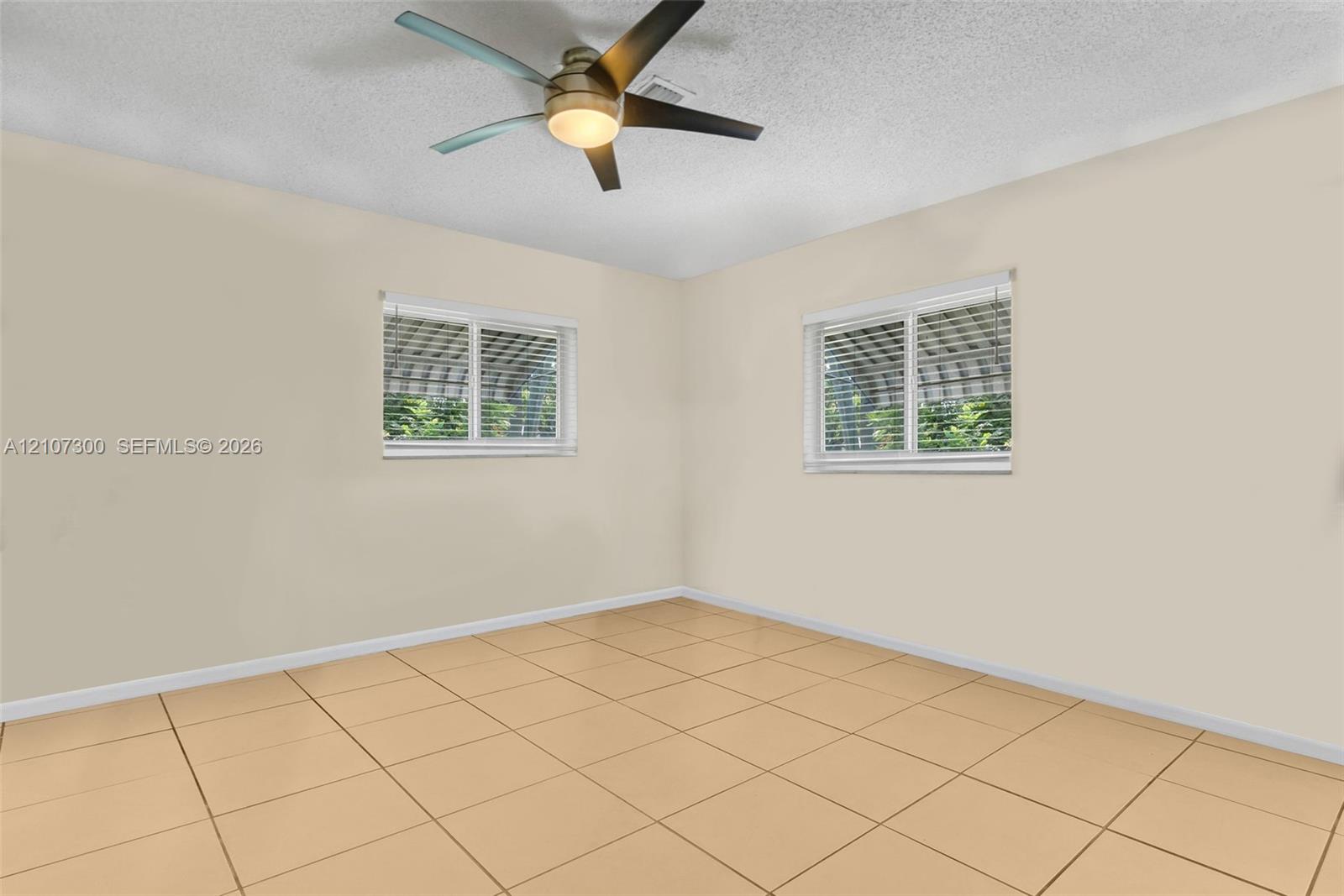 Neutral interior featuring tile flooring, two windows with horizontal blinds, and a central ceiling fan with integrated lighting