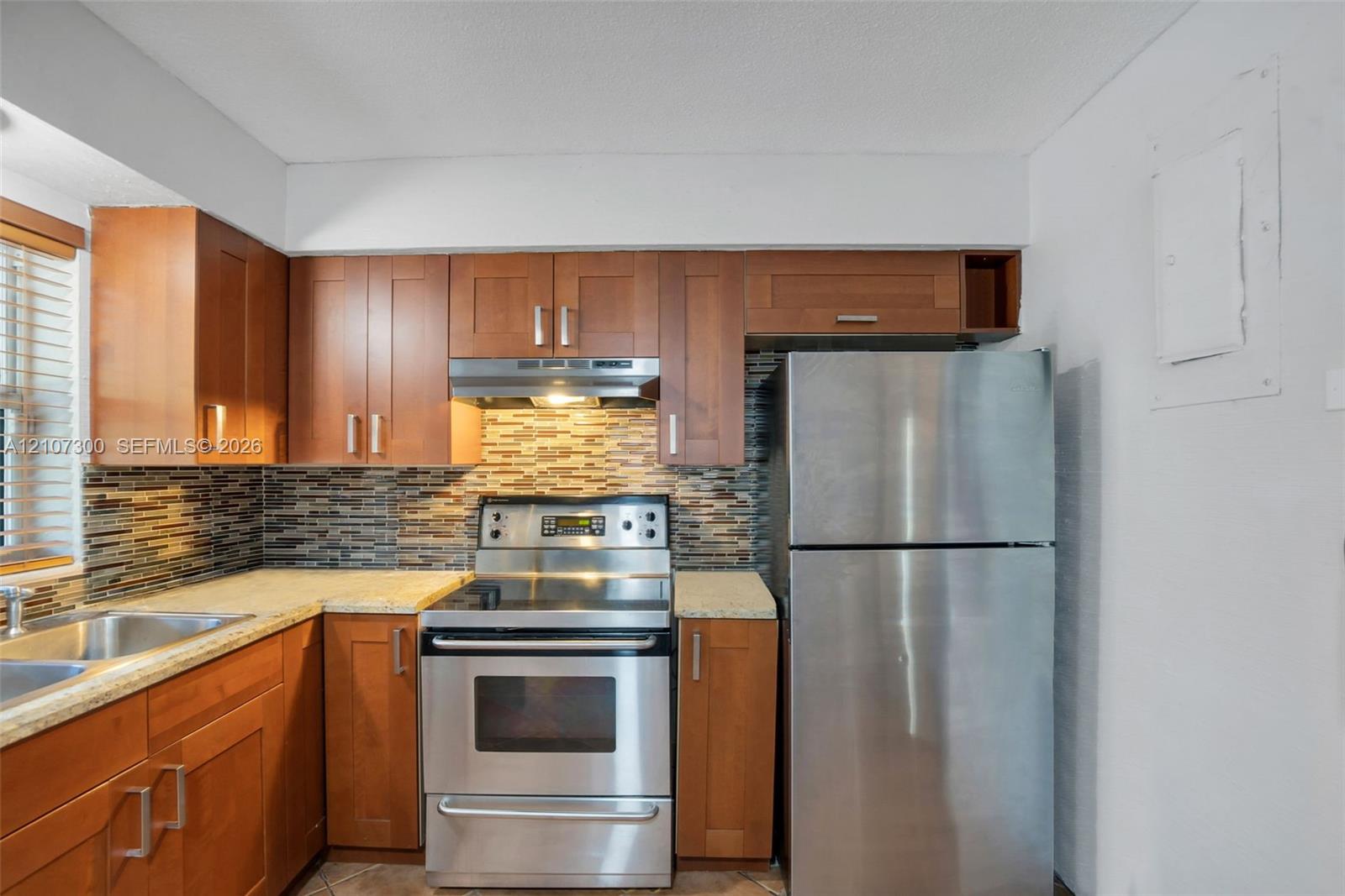 Kitchen featuring warm-tone wood cabinetry, stone-finish countertops, stainless steel appliances, and a horizontal mosaic tile backsplash