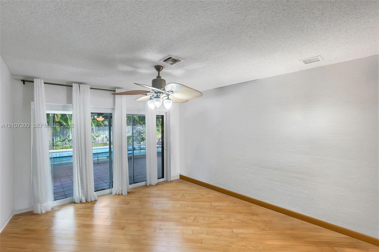 Wood-finish flooring, textured ceilings, ceiling fan with integrated lighting, and glass sliding doors featuring exterior access