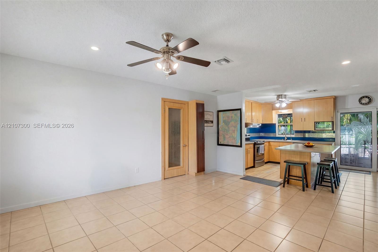 Open-concept interior featuring light-toned cabinetry, a stone-topped kitchen island, recessed lighting, ceiling fans, and neutral floor tiling