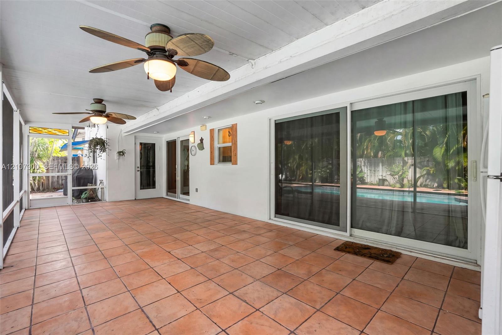 Covered patio featuring terracotta tile flooring, two ceiling fans with integrated lighting, and multiple sliding glass door entries