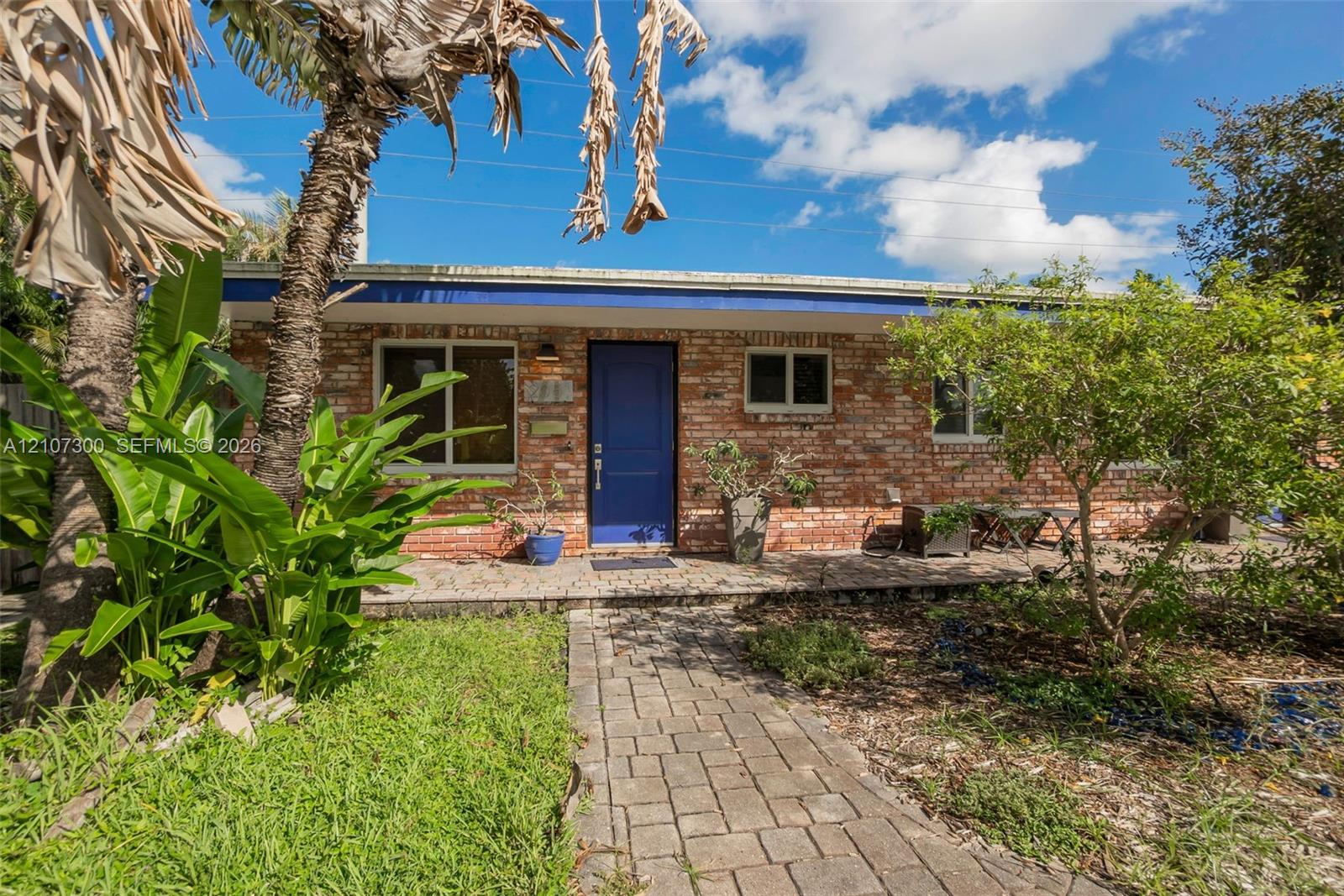 Exterior elevation featuring a red brick facade, blue entry door, stone-paver walkway, and a flat roofline