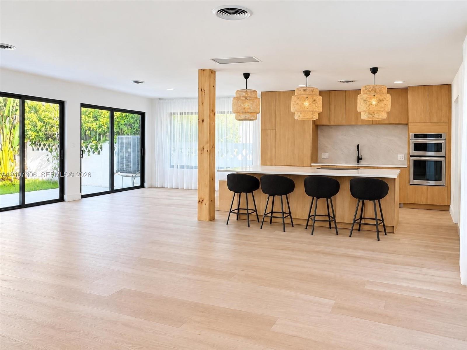 Kitchen featuring flat-panel wood cabinetry, a central island with a solid-surface countertop, built-in double ovens, wood-finish flooring, and dual sliding glass doors