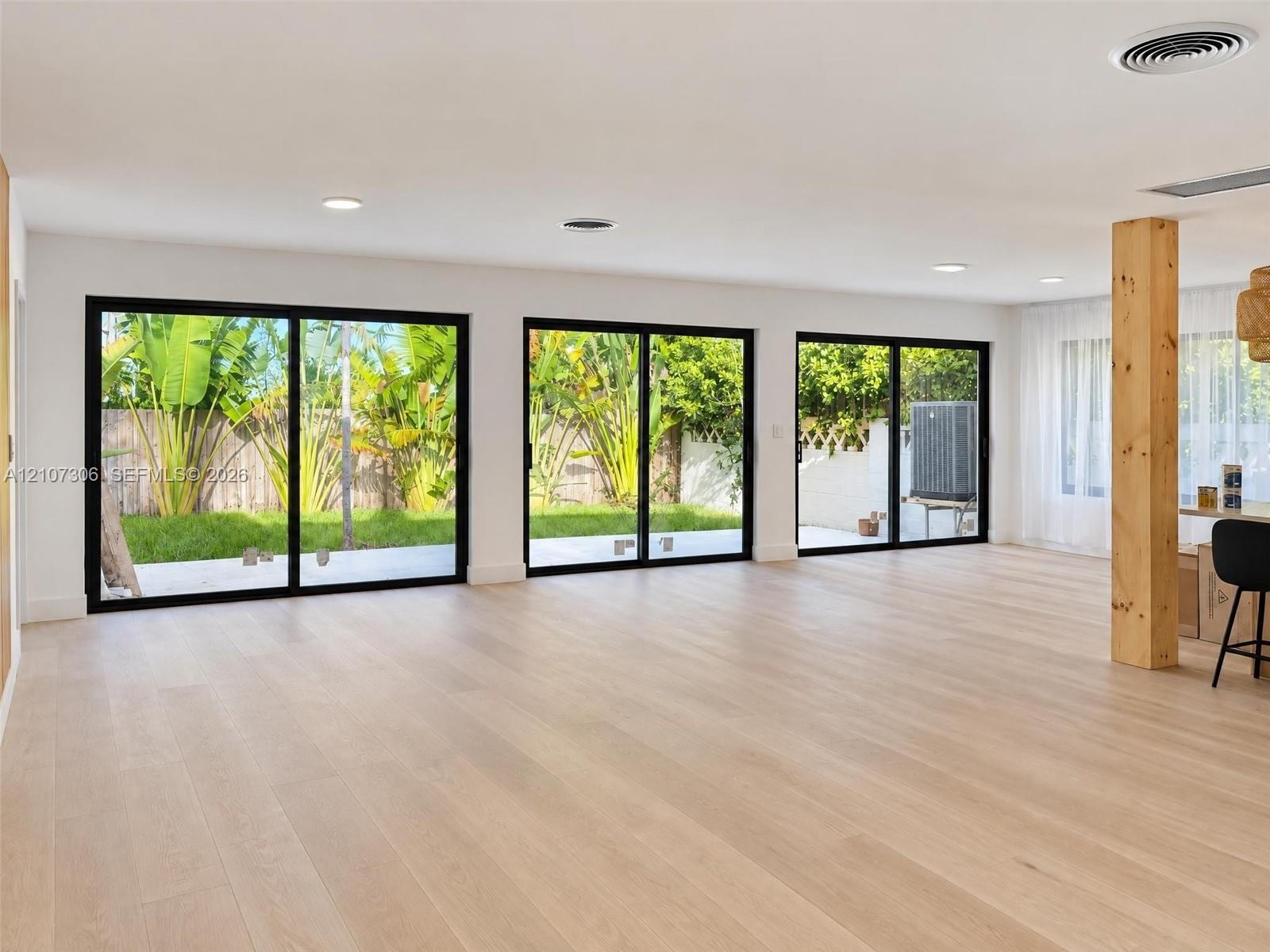 Interior space featuring three sets of black-framed sliding glass doors, light-toned wood-finish flooring, recessed ceiling lighting, and an exposed structural wood post