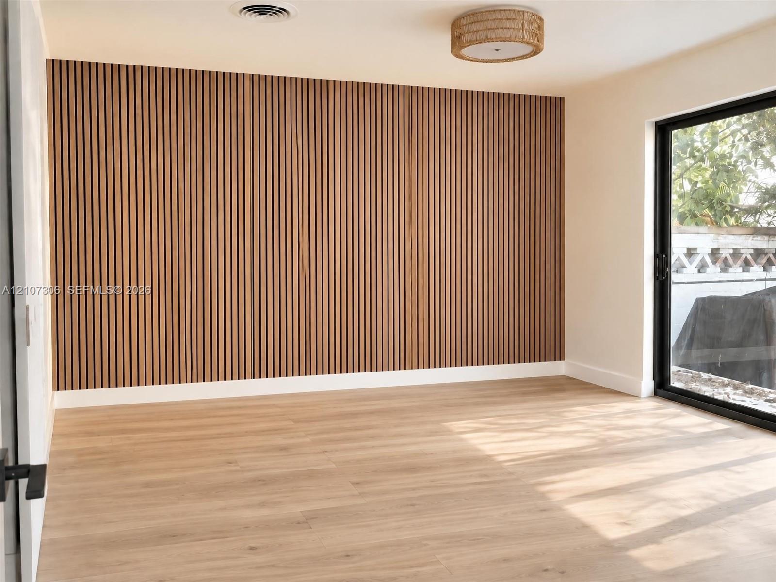 Vertical wood slat accent wall, light-toned wood-finish flooring, sliding glass door, and integrated circular drum lighting fixture