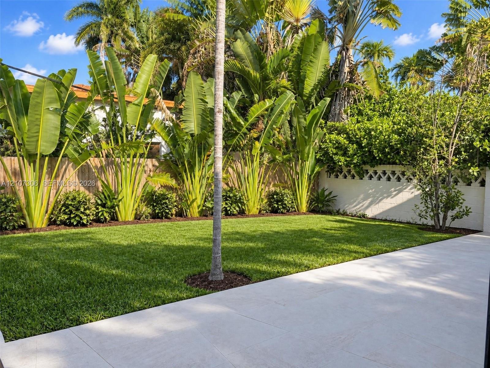 Private backyard featuring a paved stone patio, manicured lawn, established perimeter landscaping, and a decorative concrete masonry wall