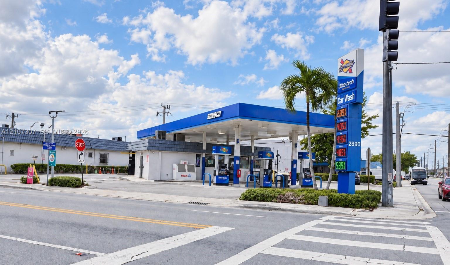 Commercial corner lot featuring a service station with a fuel canopy, paved exterior, dedicated car wash facility, and prominent roadside signage