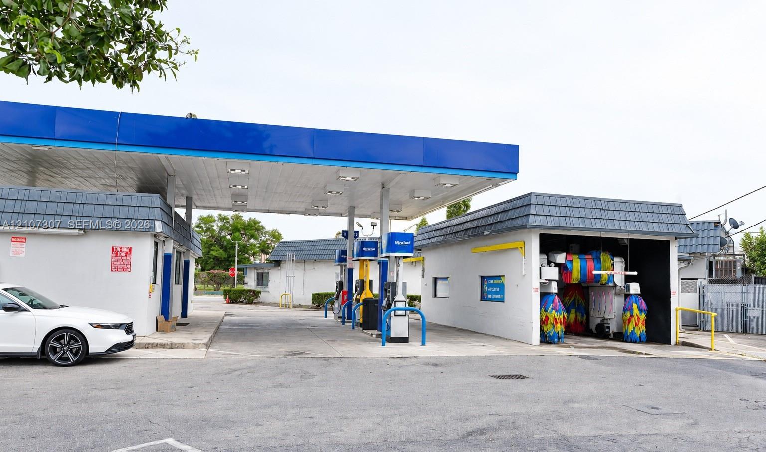 Commercial fuel station facility featuring a multi-pump canopy, integrated automated car wash bay, paved drive lanes, and masonry construction