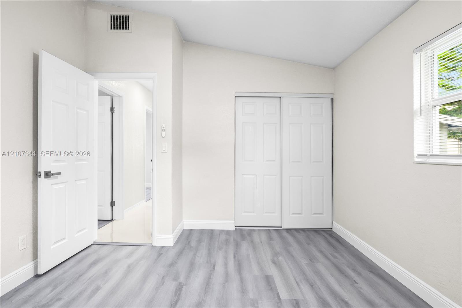 Room featuring wood-finish flooring, a vaulted ceiling, sliding-panel closet doors, and a single-hung window with horizontal blinds