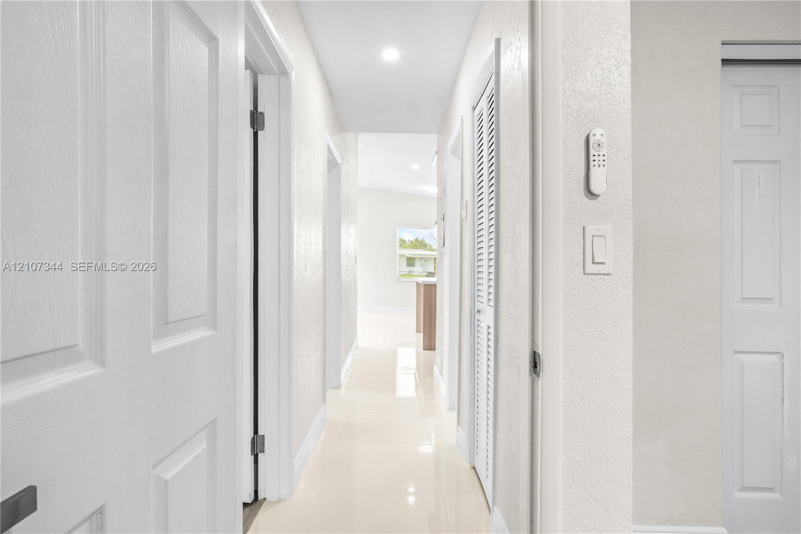 Hallway featuring light-toned tile flooring, recessed ceiling lighting, and crisp white interior doors with louvered closet paneling