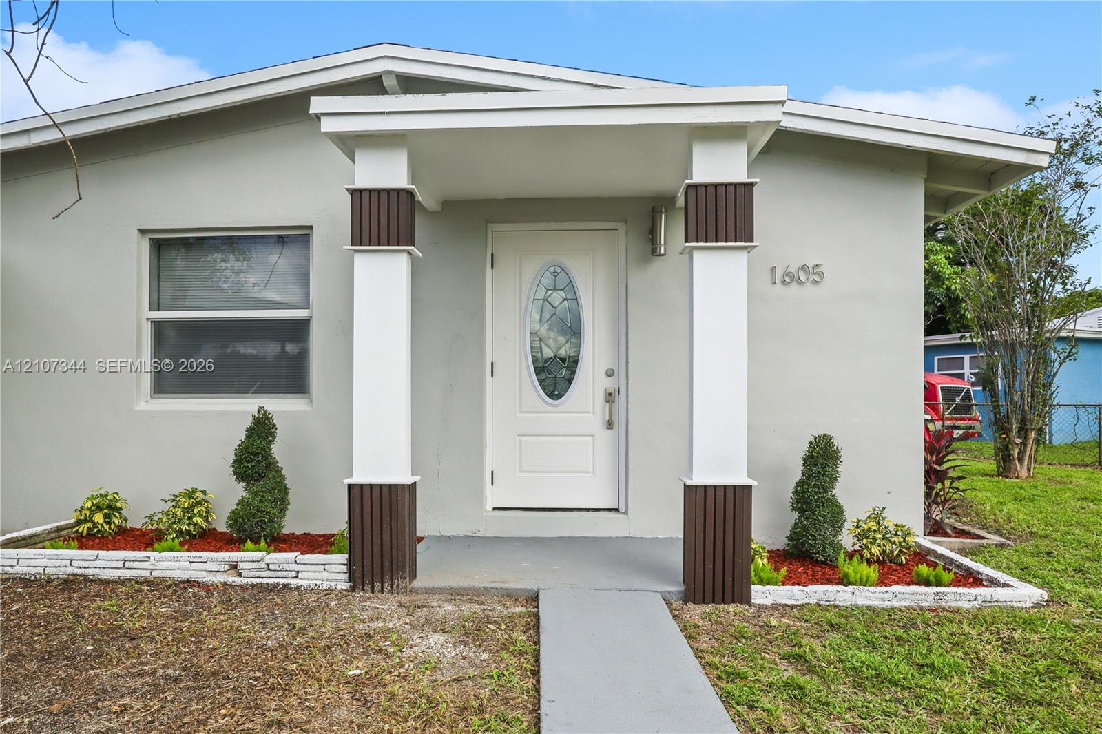 Exterior entrance featuring a covered porch, two columns with wood-toned fluted detailing, and a white front door with an oval glass insert