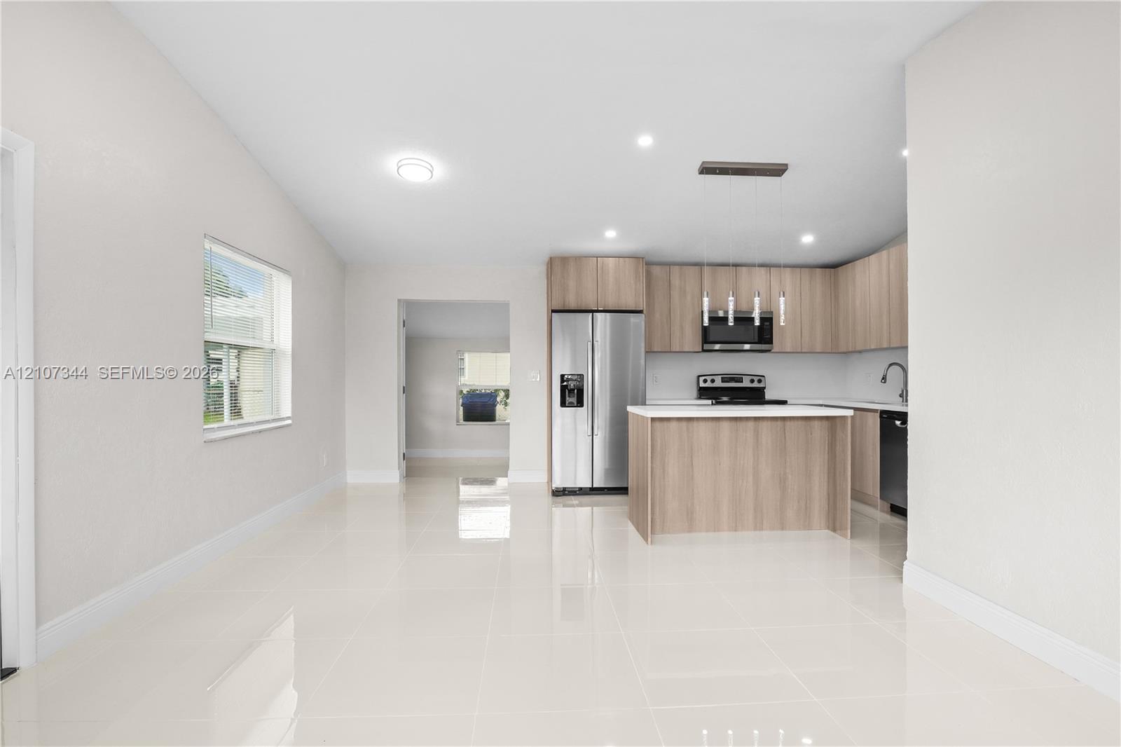 Kitchen featuring wood-finish cabinetry, stainless steel appliances, a central island with white countertop, and polished tile flooring